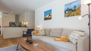En moderne stue med sofa, sofabord, stol og et køkken i baggrunden.