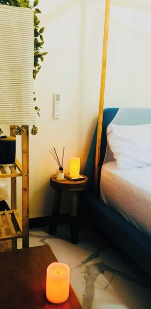 A room with a bed, a small table with a candle, a wall-mounted thermostat, and a plant. - Almadies Luxurious 2bed apartment with Ocean view (Dakar)