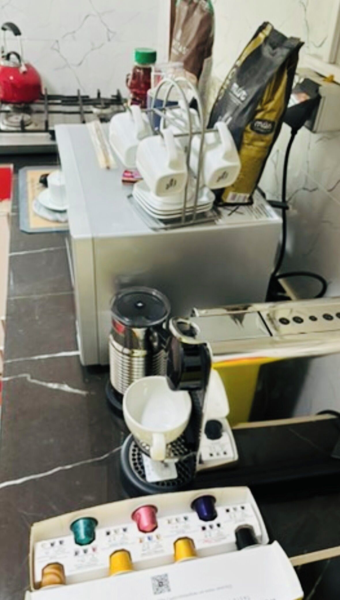 A kitchen area with a coffee machine, a kettle, a coffee maker, and a bag of coffee.