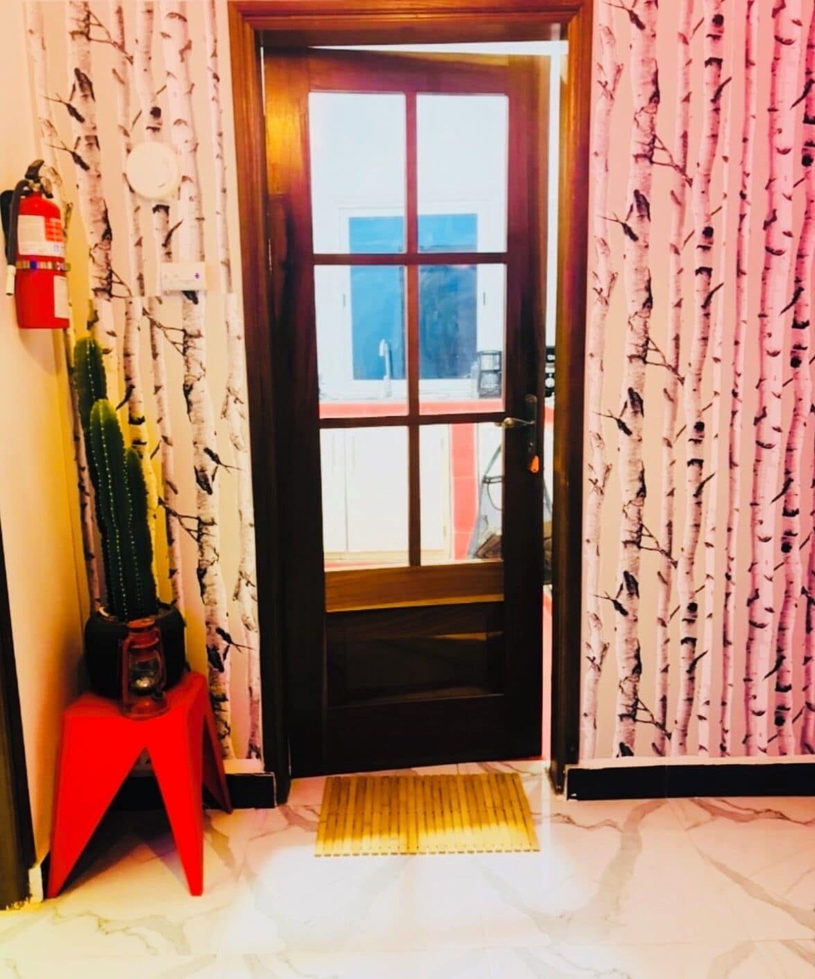 A hotel entrance with a wooden door, a red stool, and a cactus decoration.
