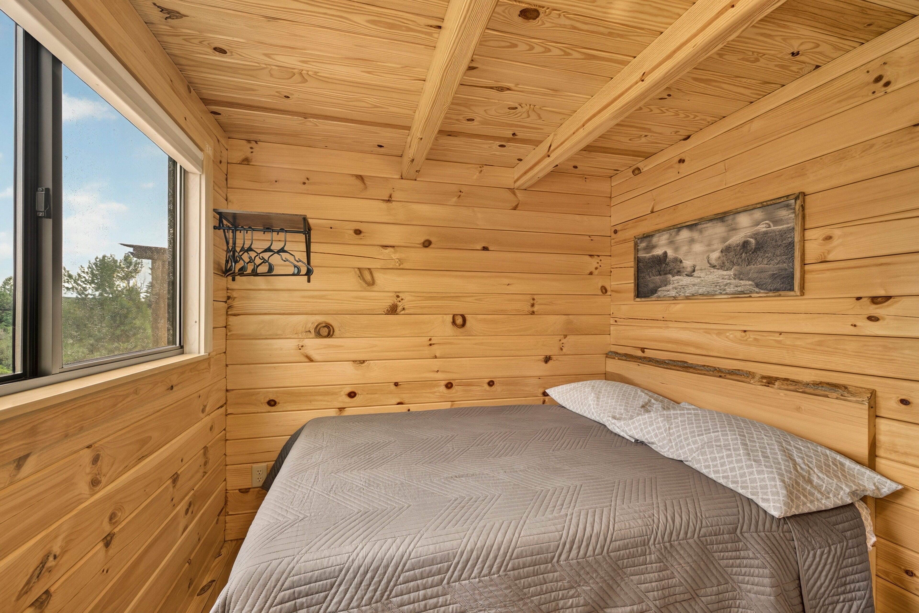 A wooden cabin room with a bed, a window, and a painting on the wall.