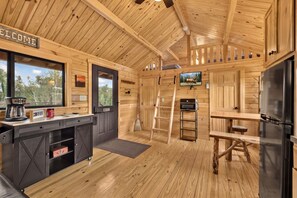 Ein Holzblockhaus-Interieur mit Küche, einer Willkommensschild, einer Kaffeestation, einer Himmelsleiter und einem Fernseher.