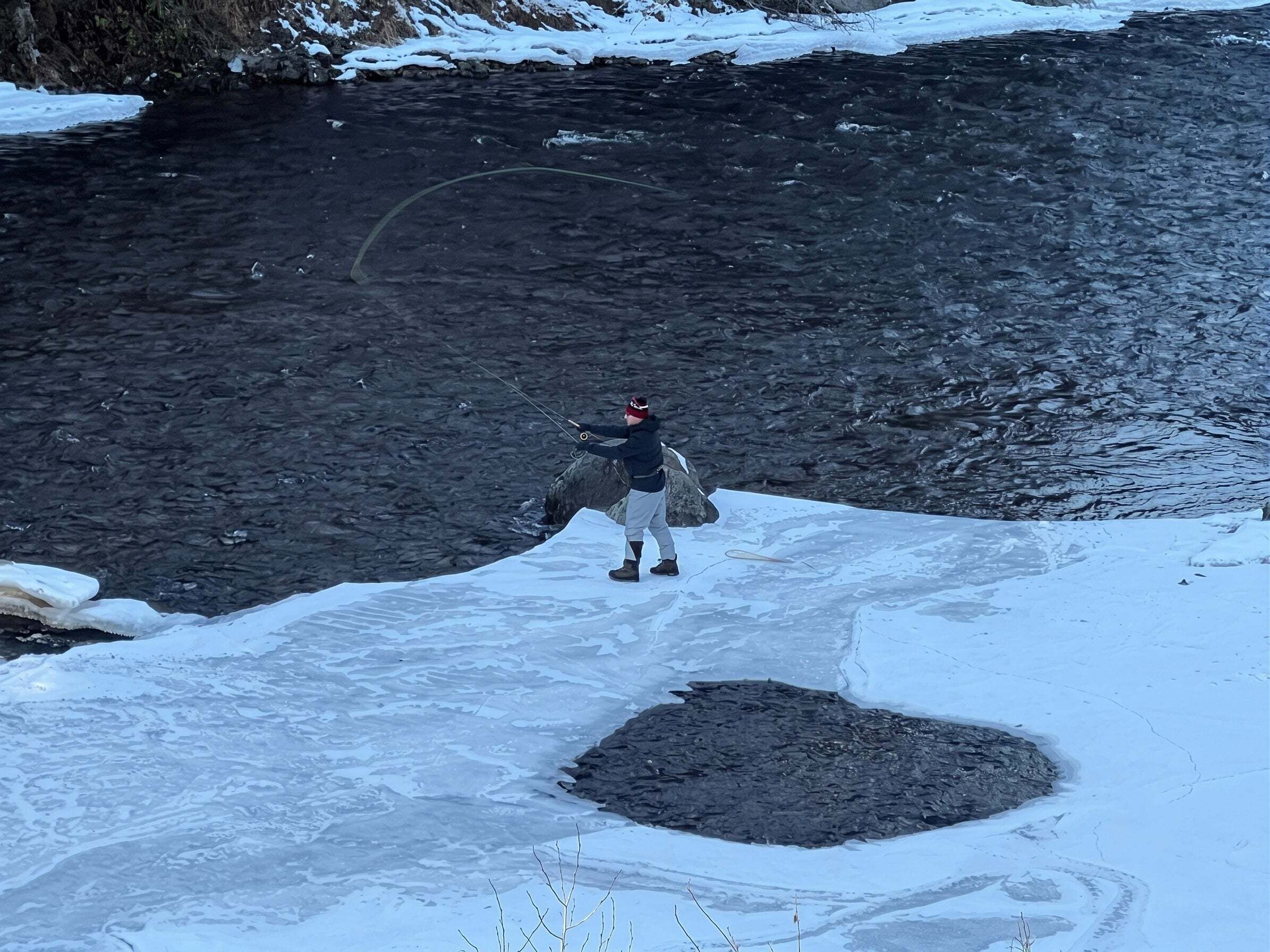 Una persona pescando en un río rodeado de hielo y nieve.
