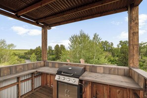 An outdoor kitchen with a grill, wooden deck, and a view of a river and forest. - 2BR cabin near water, mountains, and outdoor adventure. (Ashton)