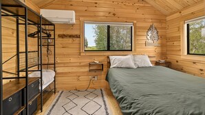 Un dormitori de cabana de fusta amb lliteres, un llit, una finestra i aire condicionat fixat a la paret.
