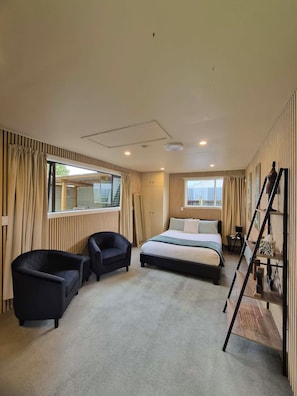 Un dormitorio con cama, dos sillones, un escritorio, una escalera y una ventana con cortinas.