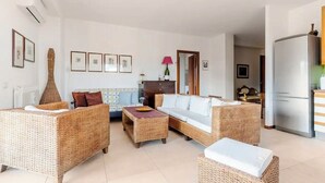 Uma sala de estar com móveis de vime, um sofá, uma mesa de centro e um espaço de refeições.