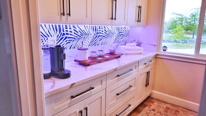 A kitchen with white cabinets, a coffee maker, and a window with a view of greenery.