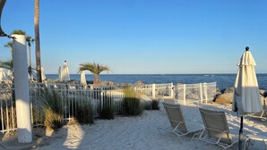A sandy beach with white umbrellas and chairs, a white fence, and a view of the ocean. - Cozy 1-bedroom condo in private Seabrook Island with 2 queen beds. (Seabrook Island)