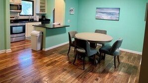 Uma cozinha compacta com eletrodomésticos modernos, uma área de refeições com mesa e cadeiras redondas, e vista para o exterior através de uma janela.
