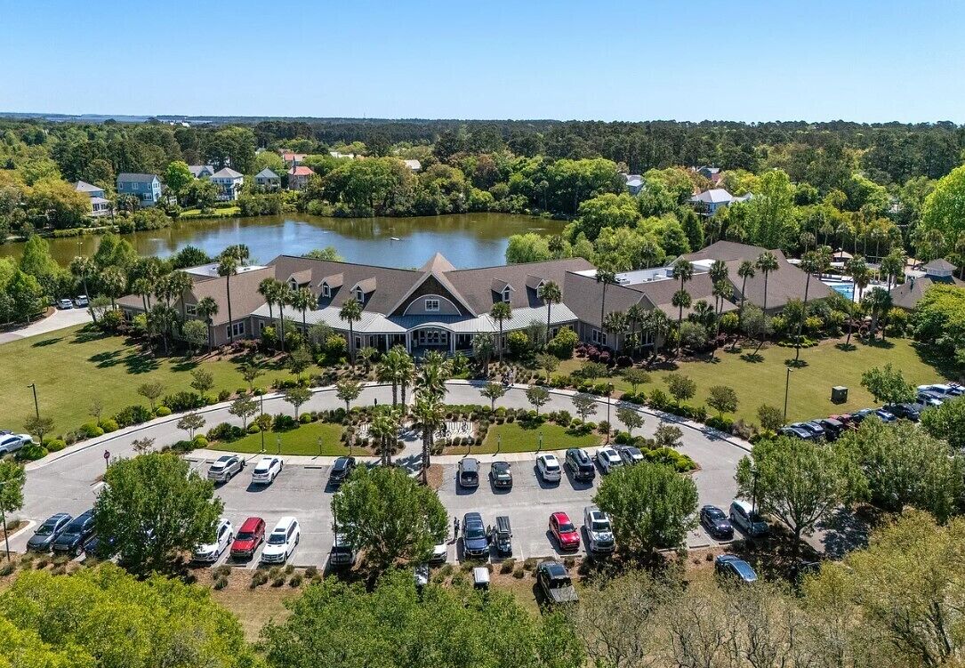 An aerial view of a hotel with a central building, a parking lot, and a lake in the background.