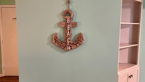 A room with a light blue wall, a wooden anchor decoration spelling 'BEACH,' a white cabinet, and a wooden floor. - Cozy 1-bedroom condo in private Seabrook Island with 2 queen beds. (Seabrook Island)