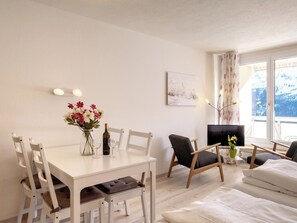 Ein modernes Wohnzimmer mit Esstisch, Stühlen, einer Couch, einem Fernseher und einem Fenster mit Blick.