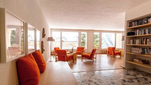 A spacious living area with a wooden floor, orange chairs, a bookshelf, and large windows. - Utoring Hohe Promenade 109&110 Appartement/Fewo, Dusche, WC, 4-Bettwohnung by Interhome (Arosa)