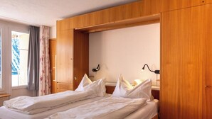 A double bed with wooden headboard, a bedside table, and a lamp. - Utoring Hohe Promenade 109&110 Appartement/Fewo, Dusche, WC, 4-Bettwohnung by Interhome (Arosa)