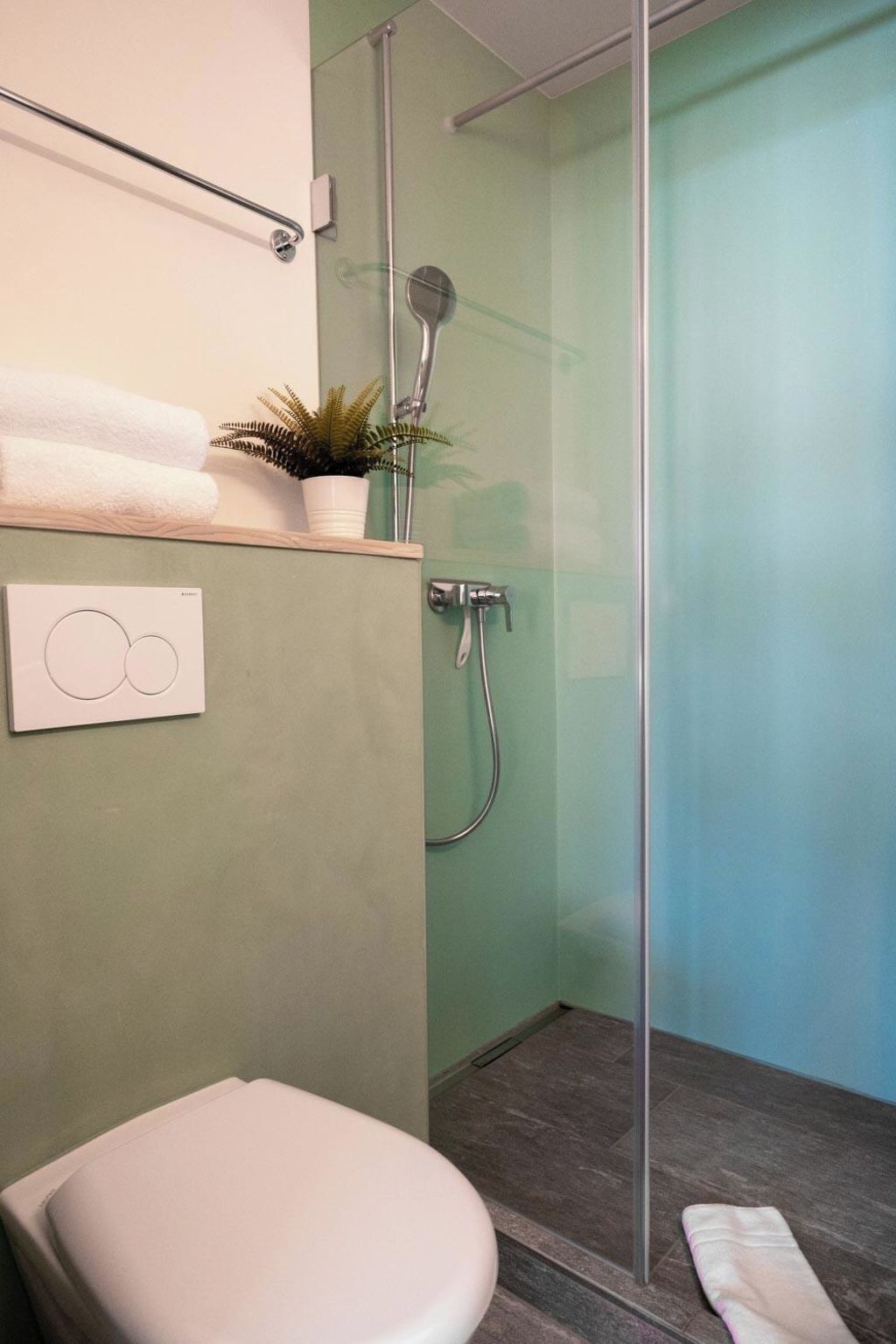 Un baño moderno con cabina de ducha de vidrio, inodoro blanco y repisa con toallas y planta.