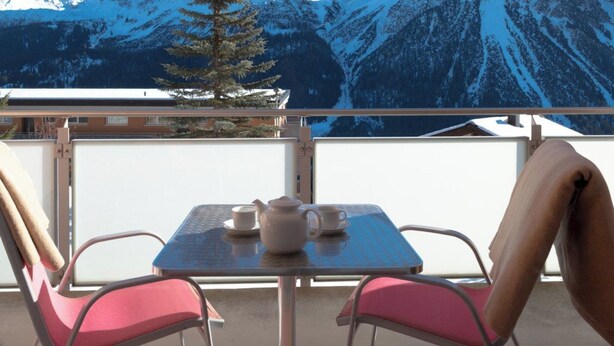 A balcony with a table and chairs, a view of snow-covered mountains, and a pine tree. - Utoring Hohe Promenade 110 Appartement/Fewo, Dusche, WC, 2-Bettwohnung by Interhome (Arosa)