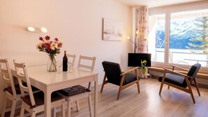 A dining area with a table, chairs, a vase with flowers, a bottle, and a TV. - Utoring Hohe Promenade 110 Appartement/Fewo, Dusche, WC, 2-Bettwohnung by Interhome (Arosa)