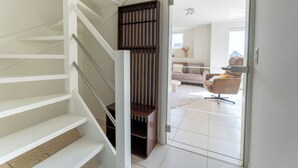 Un interno moderno con una scala, una parete rivestita in legno e vista su un soggiorno con divano e poltrona.
