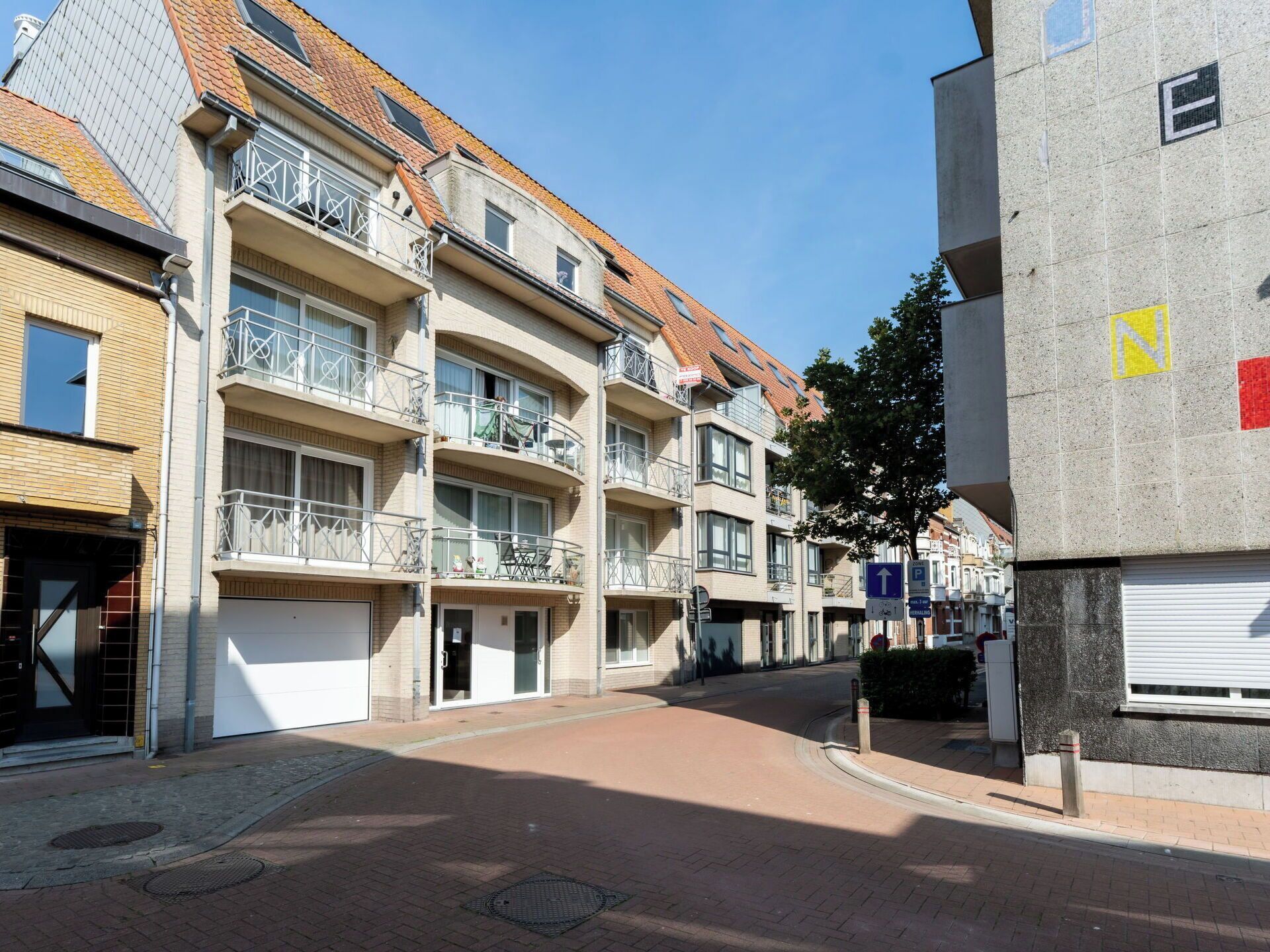 Ein mehrstöckiges Wohngebäude mit Balkonen, einer gepflasterten Straße und blauem Himmel.
