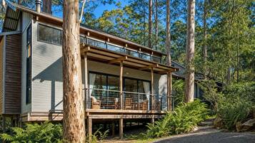 A modern wooden cabin with a balcony, surrounded by trees.