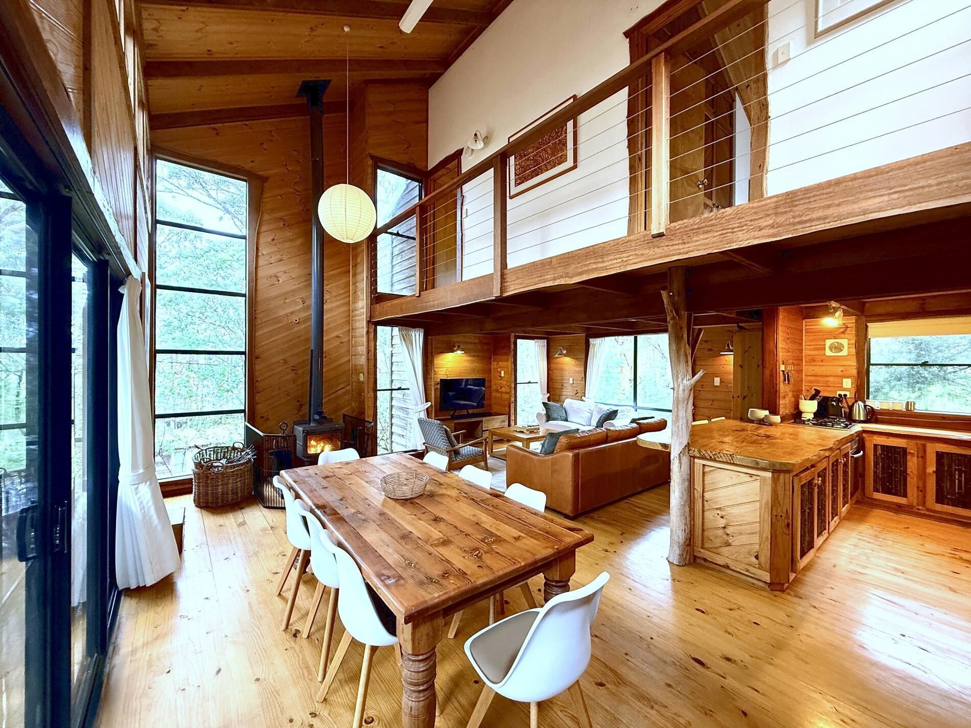 A spacious cabin with a wooden interior, a dining area, a living room with a fireplace, and a kitchen area.