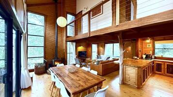 A spacious cabin with a wooden interior, a dining area, a living room with a fireplace, and a kitchen area.