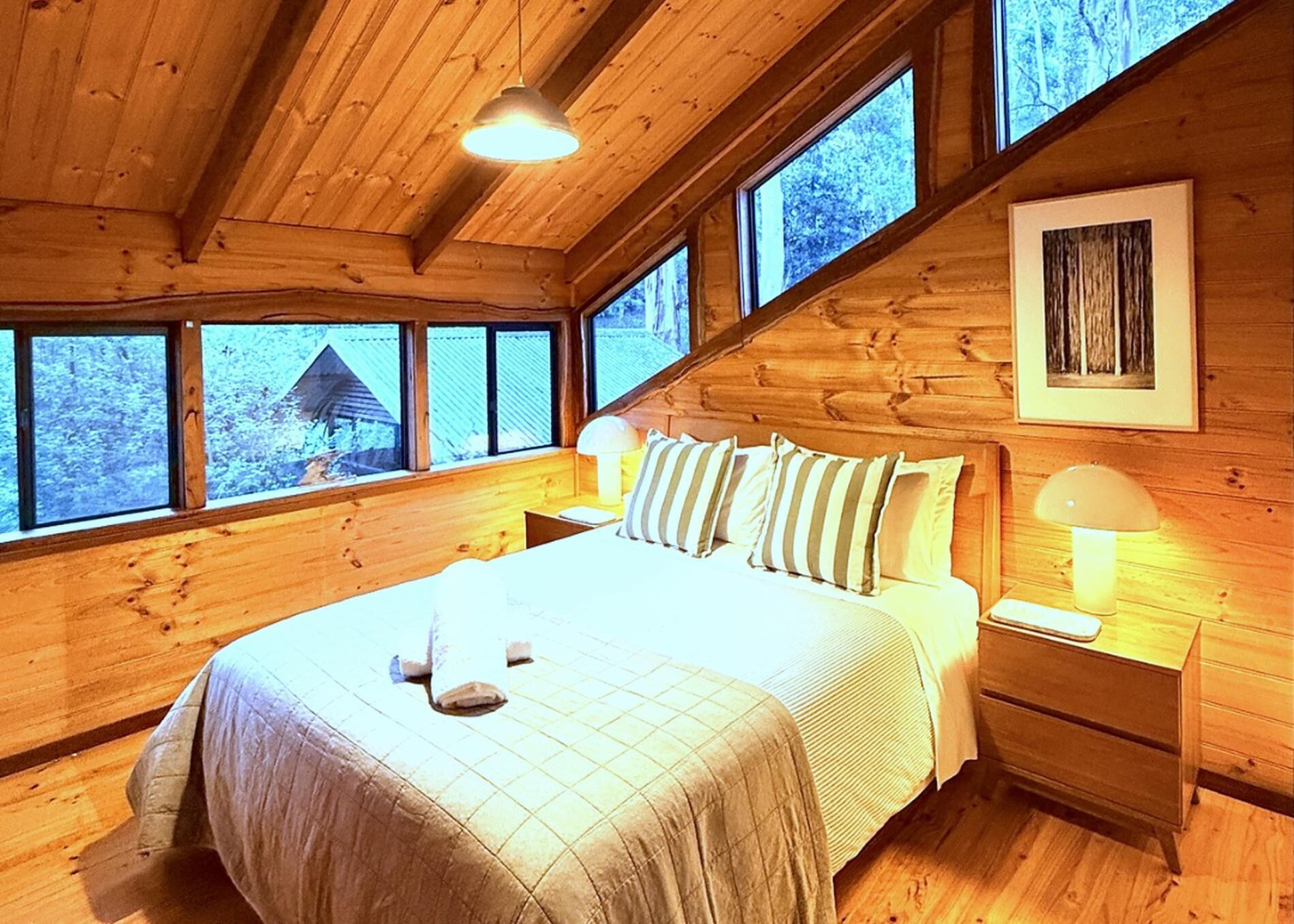 Une chambre dans une cabane en bois, avec un lit, des tables de chevet et une fenêtre donnant sur le paysage.