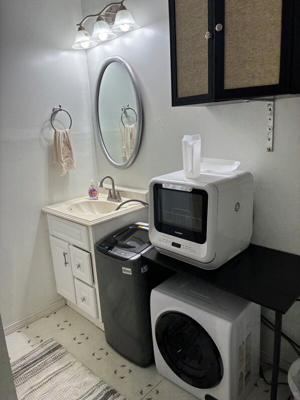 A compact bathroom with a sink, mirror, towel rack, and a washing machine.