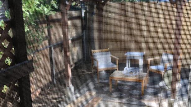 Un espacio de estar al aire libre cubierto con mesas y sillas, rodeado de follaje.