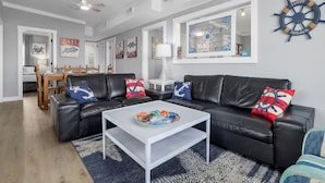 Una sala de estar con un sofá de cuero negro, una mesa de centro blanca y decoración de pared con motivos náuticos.