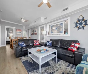 Ein Wohnzimmer mit schwarzem Ledersofa, einem weißen Couchtisch und einer Wanddekoration im Marine-Stil.