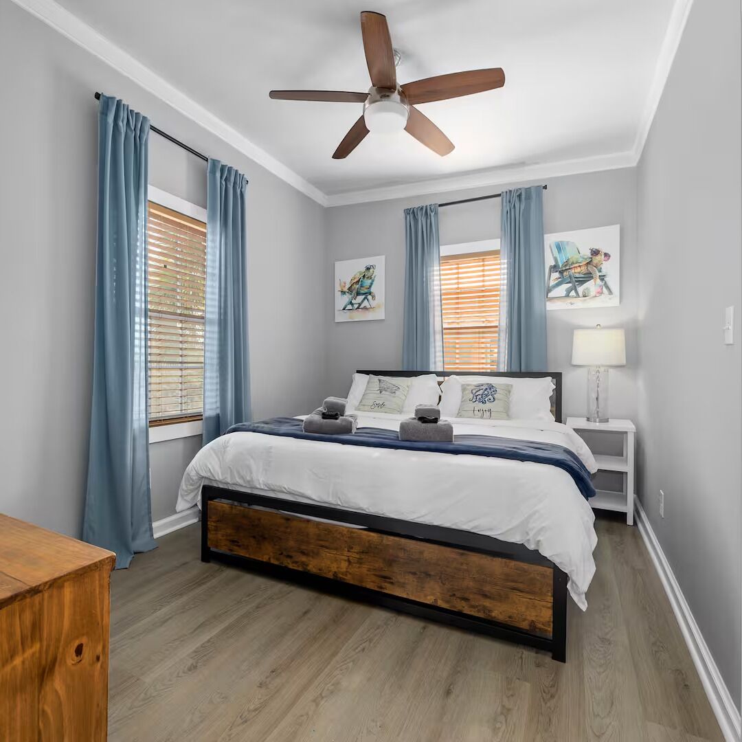 A bedroom with a bed, a ceiling fan, a nightstand, and artwork on the walls.