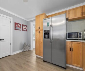 Eine Küche mit einem Edelstahl-Kühlschrank, Holzschränken, einer Mikrowelle und einer weißen Tür.