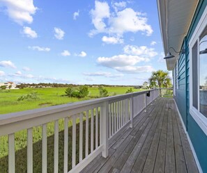 A wooden deck with a white railing overlooking a green field and a clear sky. - Classic Dreams | 4BR Marsh Oasis Near the Beach (North Myrtle Beach)