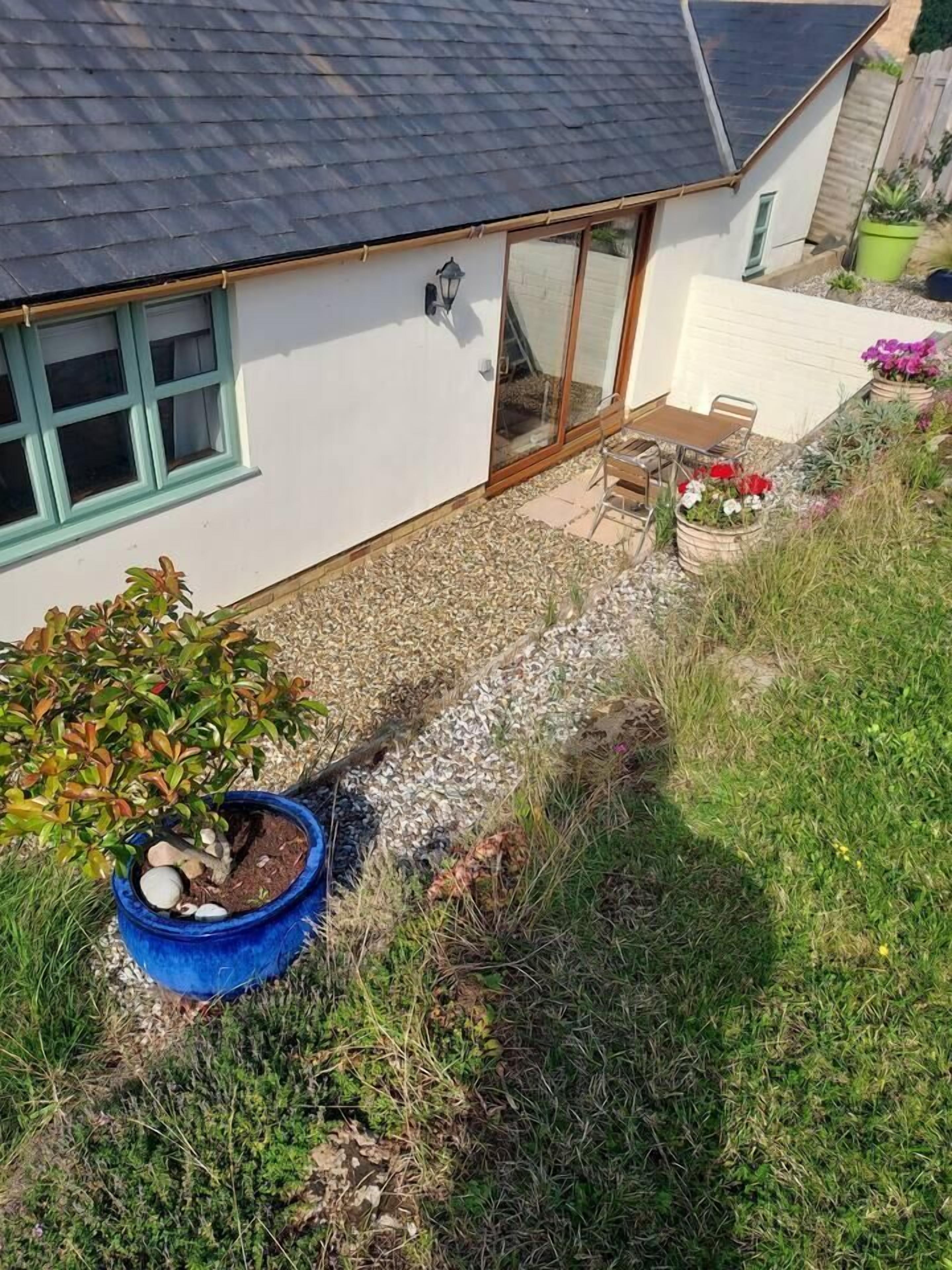 A house with a gravel patio, a blue pot with plants, and a small garden area.