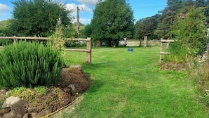 A well-maintained grassy yard with a wooden fence, a small garden bed, and a clear sky.