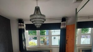 A bedroom with a large bed, a chandelier, a window with curtains, and a wooden wardrobe.