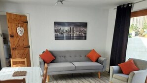 A living room with a grey sofa, two armchairs, a wooden dining table, and a cityscape painting on the wall.