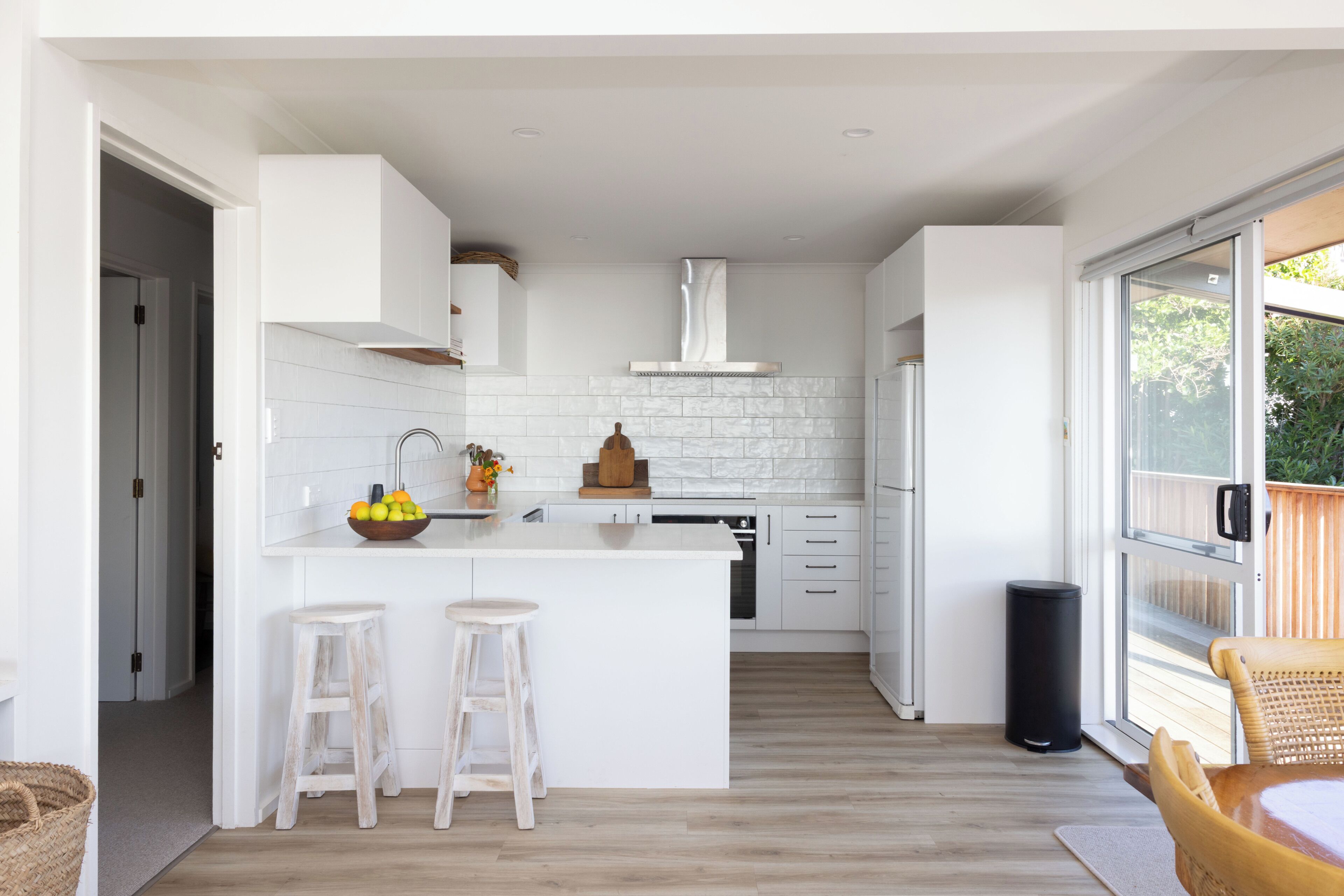 A modern kitchen with white cabinetry, a central island with stools, a built-in oven, and a large window.