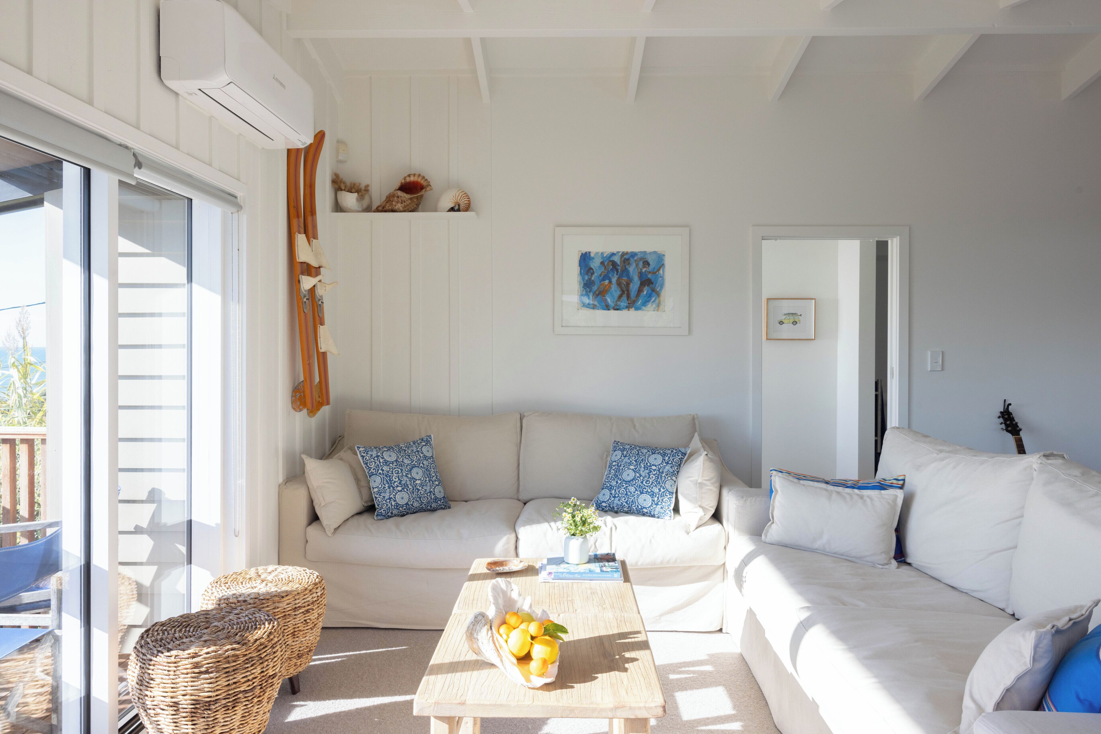 A living room with a sofa, a coffee table with fruit, a wicker chair, and a guitar in the background.