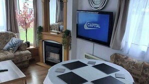 Una sala de estar con chimenea, un televisor mostrando 'CAPITAL' y una mesa redonda con tabletas.