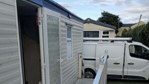 Una casa móvil con porche cubierto y una camioneta blanca estacionada al fondo.