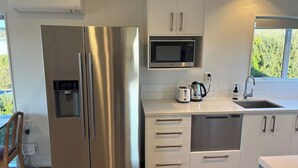 A modern kitchen with stainless steel appliances, a water dispenser, a microwave, and a sink. - Spacious Waimārama Beach House with Large Deck (Waimārama)