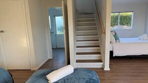 A room with a bed, a blue upholstered bench, a white towel, a staircase, and a window with a view. - Spacious Waimārama Beach House with Large Deck (Waimārama)