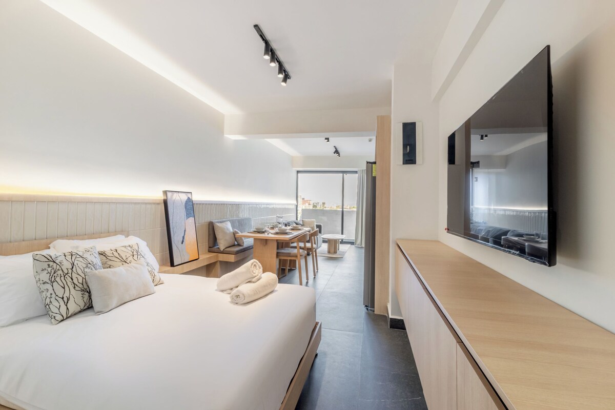 Habitació d'hotel amb llit, zona de dinar i televisió penjada a la paret.