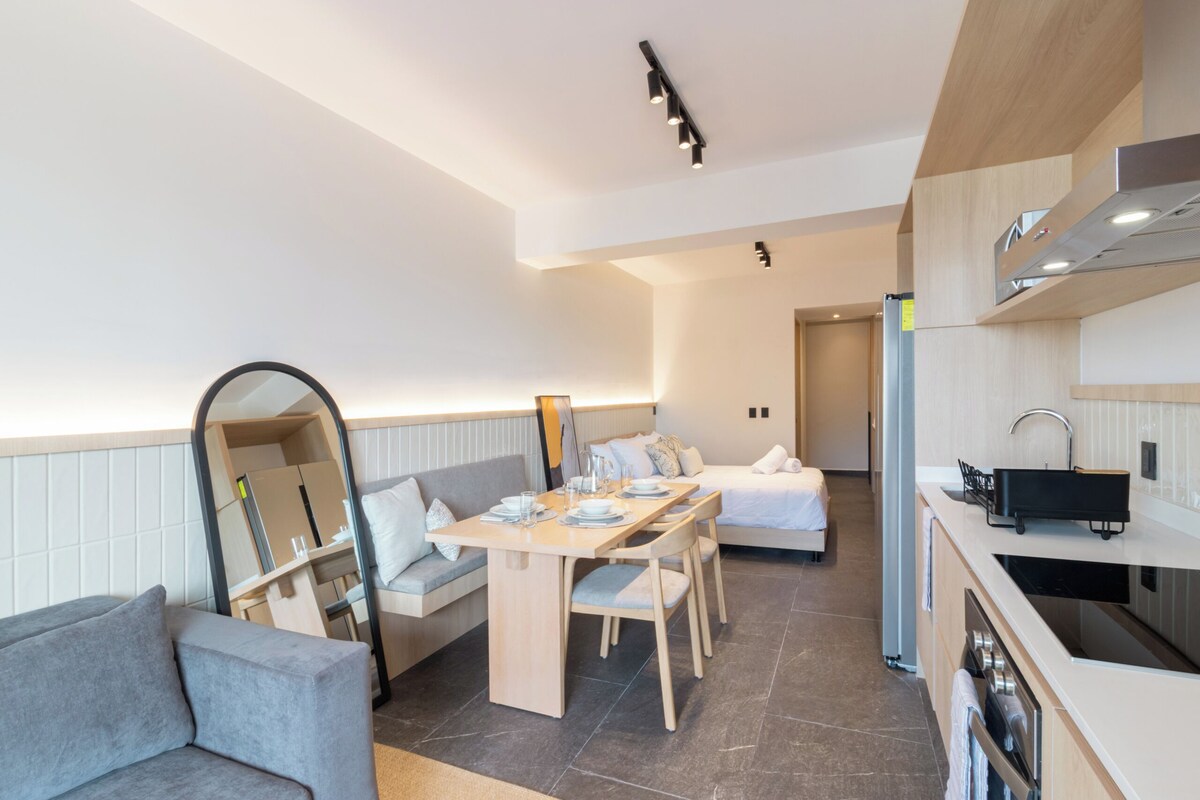 Ein modernes Hotelzimmer mit Essbereich, einer Couch, einem Spiegel und einer Küchenzeile.