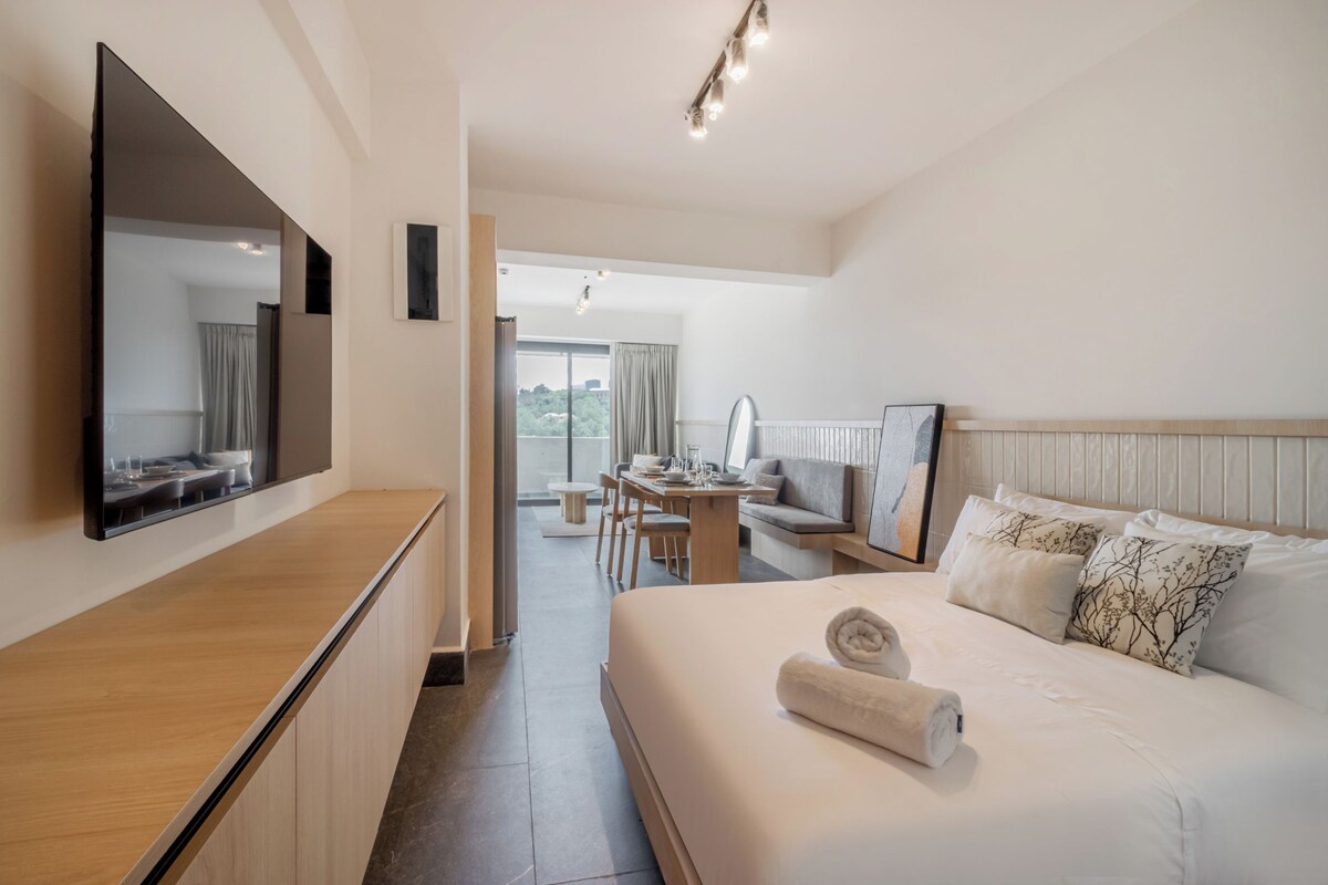 Habitació d'hotel amb llit, escriptori, cadira, televisió de pantalla plana penjada a la paret i vista cap a l'exterior.