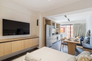 Ein modernes Hotelzimmer mit Fernseher, Essbereich mit Tisch und Stühlen, einer Küchenzeile und einer Sitzecke.