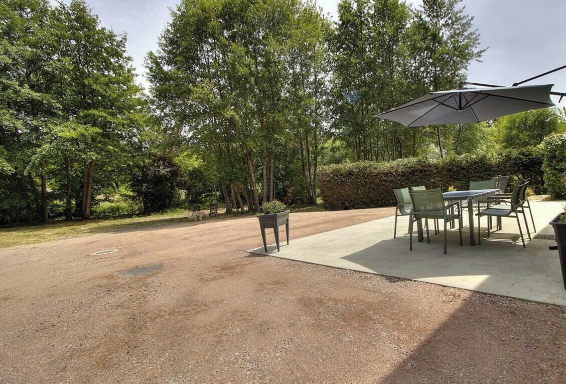 A gravel patio with a table and chairs, surrounded by trees and a hedge.